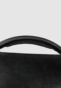 Zwarte leren handtas met een gladde textuur, voorzien van een afgeronde handgreep en contrasterende stiksels langs de rand.