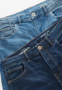 Două perechi de blugi skinny: una de un albastru deschis, cealaltă de un albastru închis. Ambele au cinci buzunare, cusături maro și nasturi metalici la talie.