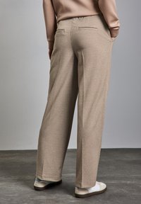 Pantaloni beige a quadri con gamba dritta, dotati di due tasche posteriori e cintura elastica. Abbinati a sneakers bianche.