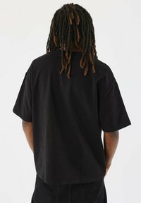 Camiseta negra de gran tamaño hecha de algodón, con un corte relajado y mangas cortas. La parte posterior es lisa, sin patrones ni acentos visibles.