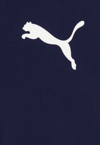 Jūras spēku krāsas audums ar balto lēcēju kaķa logo. Gluda tekstūra, minimālistisks dizains, kas ietver ikonisko Puma zīmolu.
