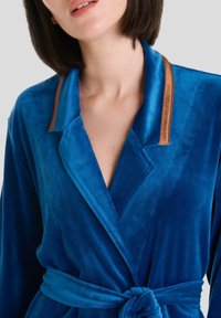 Ropa de terciopelo azul con un escote en V profundo, mangas largas y acentos de cuero marrón en el cuello. Incluye un cinturón de tela a juego.