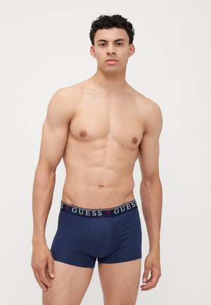 Sötétkék boxer alsónadrág márkázott, elasztikus derékpánttal, amelyen a "GUESS" logó kontrasztos színekben látható. Pamut keverék, sima tapintású.