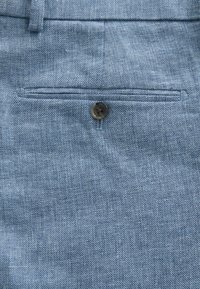 Tela azul claro con una superficie texturizada, que presenta un bolsillo trasero y un solo botón marrón para cierre.