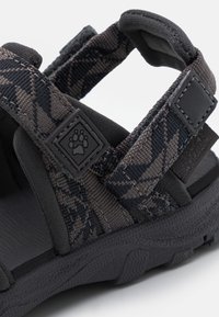 Black and gray sandal with textured fabric straps and rubber sole, featuring a paw print logo detail on the strap.