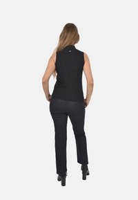 Top nero senza maniche con collo alto; design aderente. Abbinato a jeans blu scuro e stivali neri con tacco alto, visto da dietro.