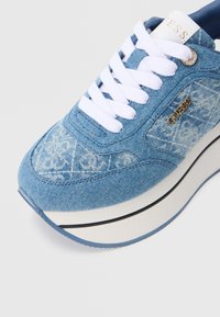 Αθλητικό παπούτσι από τζιν με ύφασμα σε ανοιχτό γαλάζιο χρώμα και διακριτικό σχέδιο, λευκά κορδόνια, χρυσή λογότυπη λεπτομέρεια και παχιά λευκή σόλα με μαύρο περίγραμμα.
