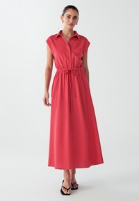 Coral maxi kjole med korte ærmer, knaplukning foran, elastisk talje og snørredetalje. Glat stof, let design og fuld længde.