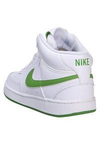 Zapatilla alta blanca con acentos verdes, que presenta una parte superior de cuero texturizado, un collar acolchado y un prominente swoosh verde de Nike.
