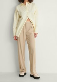 Ljusgul oversized knapp-up skjorta, beige veckade byxor och off-white loafers med svarta sulor. Enkla, avslappnade passform.