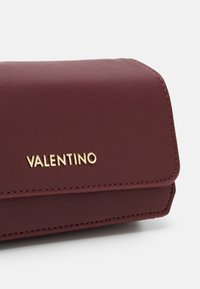 Portafoglio in pelle bordeaux con una texture liscia, caratterizzato dal logo dorato "VALENTINO" e bordi cuciti, forma rettangolare e chiusura a pattina.
