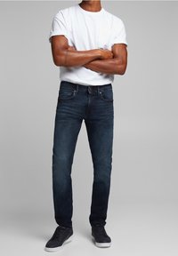 Mörkblå denimjeans i slim fit med fickor, subtila sömnadsdetaljer, och kombinerat med en vit t-shirt och svarta sneakers.