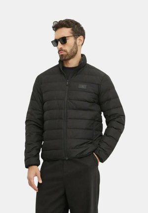 Giacca a vento nera con chiusura a zip, design trapuntato, colletto alto e un piccolo logo sul lato sinistro del petto. Tessuto dalla superficie liscia.