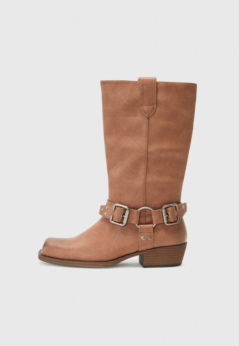 Botte mi-hauteur en cuir camel avec brides latérales à boucles et petit talon empilé, montrée de la face intérieure sur un fond gris clair.