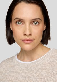 Hellbeige strukturierter Pullover mit einem weißen Kragen. Das Model hat kurzgeschnittenes braunes Haar und grüne Augen und blickt gegen einen neutralen Hintergrund.