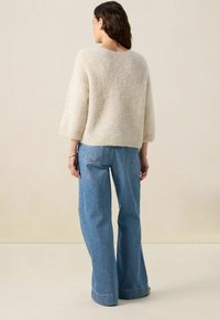 Pull en beige clair et moelleux avec des manches trois-quarts, associé à un jean bleu à taille haute, à jambes larges, avec des poches arrière et un ourlet effiloché.