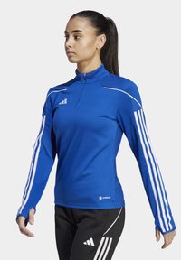 Blaues sportliches Langarmoberteil mit einem halben Reißverschluss; verfügt über weiße Streifen an den Ärmeln und einen strukturierten Kragen; besteht aus einem glatten, flexiblen Material.