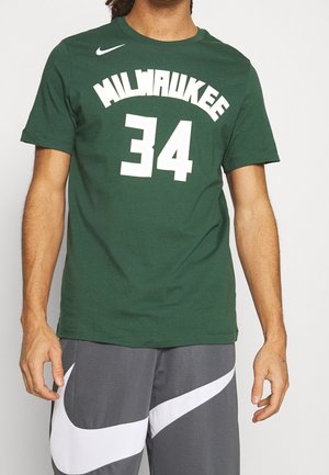 Osoba nosząca zieloną koszulkę Milwaukee z numerem 34 i szare szorty z dużym białym logo Nike swosh.