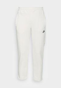 Vita träningsbyxor av mjukt material med elastisk midja, sidofickor och en grön Nike-logotyp på vänster ben.