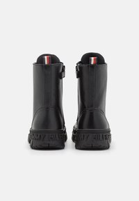 Bottines en cuir noir avec une finition texturée, dotées d'une fermeture zippée et d'une semelle en caoutchouc emboutie du logo. Accent rouge, blanc et bleu à l'arrière.