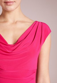 Lyhyt vaaleanpunainen mekko, jossa on roikkuva kaula-aukko, capped-hihat ja poimutettu yksityiskohta vartalon ympärillä, mikä takaa sileän istuvuuden.