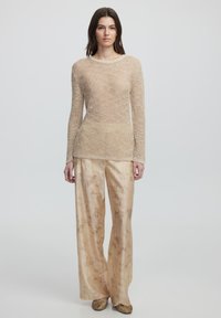 Beige Strickpullover mit langen Ärmeln und lockerer Passform, kombiniert mit hellgoldenen, weit geschnittenen Hosen mit einem dezenten floralen Muster. Strukturiertes Material.