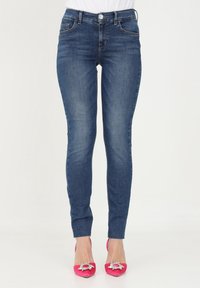 Jeans ajustados de mezclilla azul oscuro con una cintura a media altura, que cuentan con bolsillos frontales y un ligero patrón desgastado. Combinados con tacones de aguja rosas.