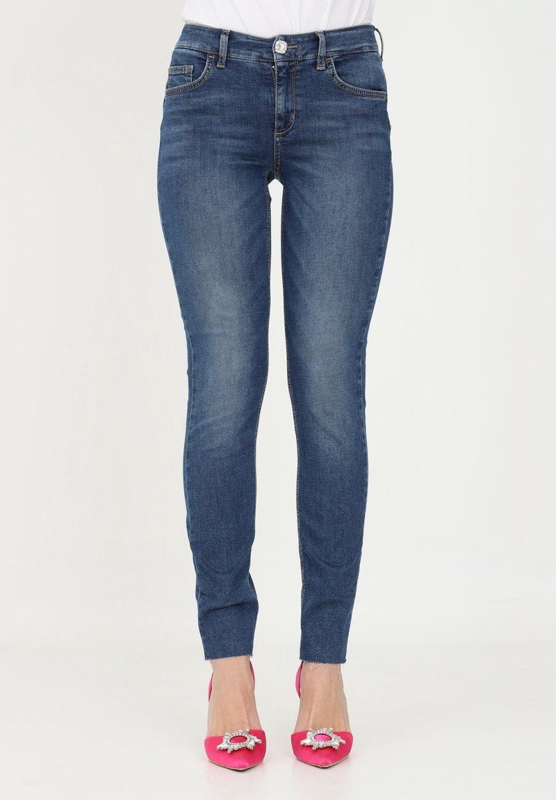 Jeans ajustados de mezclilla azul oscuro con una cintura a media altura, que cuentan con bolsillos frontales y un ligero patrón desgastado. Combinados con tacones de aguja rosas.