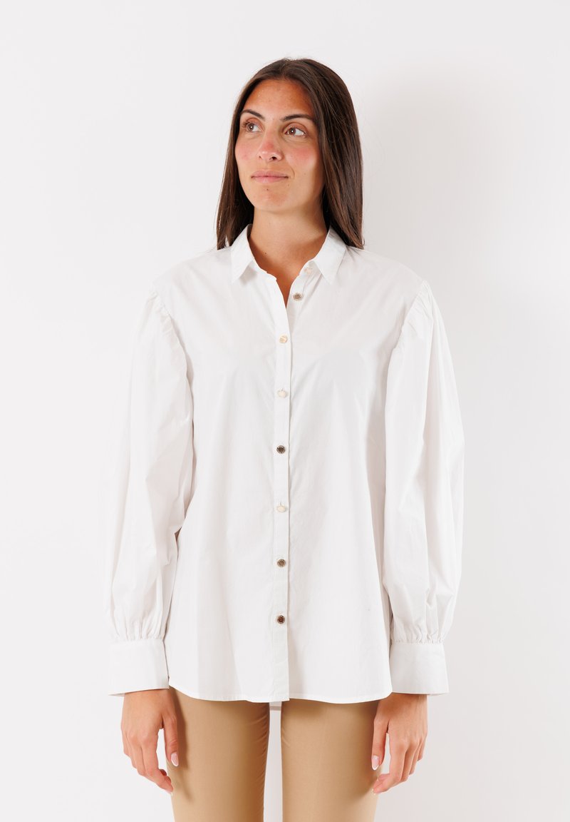 Camicia in cotone bianco con bottoni sul davanti, colletto a punta e maniche a sbuffo. Presenta bottoni beige e polsini aderenti. Texture liscia.