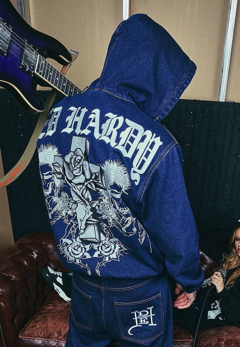 Donkerblauwe spijkerhoodie met een groot grafisch ontwerp van rozen en een kruis op de achterkant, geborduurde merknamen en een voorzakdetail.