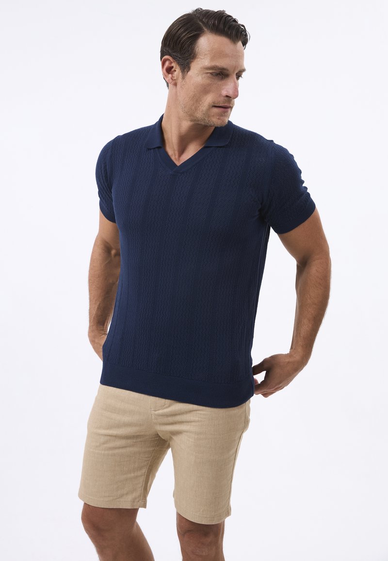 Dunkelblaues Strick-Poloshirt mit kurzen Ärmeln, strukturiertem Muster und V-Ausschnitt, kombiniert mit hellbeigen Shorts.