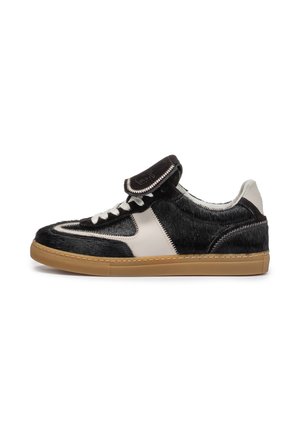 Low-top sneaker met zwart-witte gestructureerde panelen, witte veters, omgeslagen tong en rubberen zool in gumkleur, zijaanzicht op witte achtergrond.