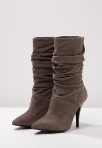 Stivaletti alla caviglia in suede grigio con un design morbido, punta affusolata e tacco stiletto alto. Superficie texture con dettaglio di materiale arricciato.