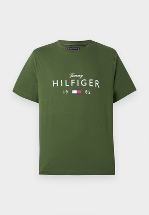 T-shirt verde in cotone con maniche corte, caratterizzato da testo bianco "Tommy HILFIGER 1985" e una piccola icona della bandiera colorata sottostante.