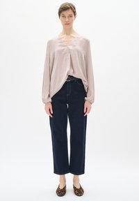 Maglietta rosa chiaro a maniche lunghe con scollo a V, abbinata a jeans blu scuro a vita alta e scarpe slip-on con stampa leopardata. Design minimalista.
