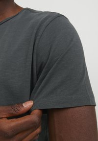 Camiseta de color gris oscuro, hecha de tela suave, con un clásico cuello redondo y un diseño de manga corta, con detalles de costura visibles.