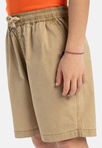 Pantalones cortos beige con cintura elástica, cordón de ajuste y bolsillos laterales. Fabricados con una tela ligera de textura suave.