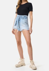 Svetle modré džíny s vysokým pasem a třepeným lemem s uvázaným páskem. Černé přiléhavé tričko a krémové kotníkové boty.