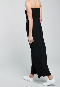 Robe maxi noire sans bretelles avec une taille élastique et une silhouette fluide, associée à des baskets blanches pour un look décontracté.