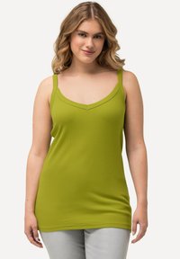 Zelený žebrovaný top bez rukávů se širokými ramínky, výstřihem do V a volným střihem, který je kombinován se světle šedými kalhotami. Hladká textura po celé ploše.
