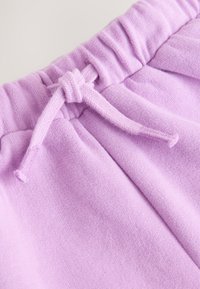 Lähikuva purppuranvärisistä pehmeistä kangashousuista, joissa on kuminauhavyötärö ja sidottu kiristysnauha.