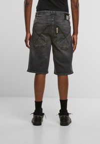 Pantalones cortos de mezclilla negra con un corte recto, costuras visibles, dos bolsillos traseros y una etiqueta en la cintura. La tela tiene una textura desgastada.