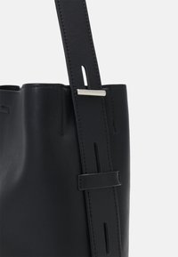 Sac fourre-tout en cuir noir à texture lisse, doté d'une large bandoulière et d'un accent métallique argenté. Design simple et fonctionnel.