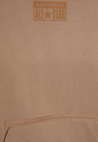 Felpa beige con tasca a marsupio e grande logo arancione di Converse All Star al centro in alto. Tessuto morbido e strutturato.