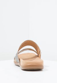 Sandale à lanières argentées avec deux bretelles fines, une semelle intérieure rembourrée couleur tan, et une semelle extérieure solide marron clair. Texture lisse et design minimaliste.