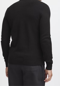 Czarny sweter z teksturowanym wzorem w kratkę typu waffle. Posiada okrągły dekolt oraz ściągacze na mankietach i u dołu. Widok od tyłu.