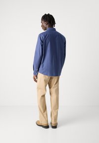 Blauw overhemd met lange mouwen, beige broek, effen stof, tailored fit en eenvoudig patroon. Achteraanzicht toont de lengte en de pasvorm van het shirt.