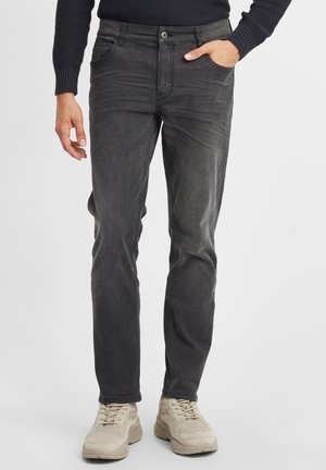Jean en denim gris slim fit avec une texture délavée, comportant des poches avant et une fermeture à bouton, assorti à des baskets de couleur claire.