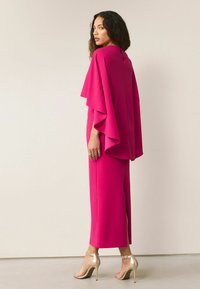 Fuksjowa bluzka w stylu peleryny z luźnymi rękawami, w połączeniu z dopasowanymi spodniami o prostym kroju. Posiada detal w postaci wycięcia na plecach oraz złote szpilki.