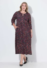 Mustapuku, jossa on värikäs paisley-kuvio, 3/4-hihat, avonainen kaula-aukko, sivutaskut ja soljuva muotoilu. Yhdistetty mustia korkokenkiä.